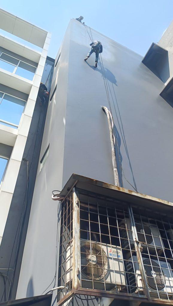 Pekerja menggunakan teknik rope access untuk pengerjaan waterproofing pada dinding luar gedung tinggi