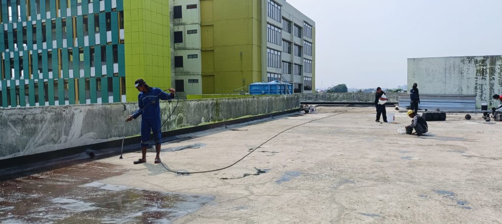 Tim profesional sedang melakukan proses waterproofing dak beton pada atap gedung sekolah di Bogor