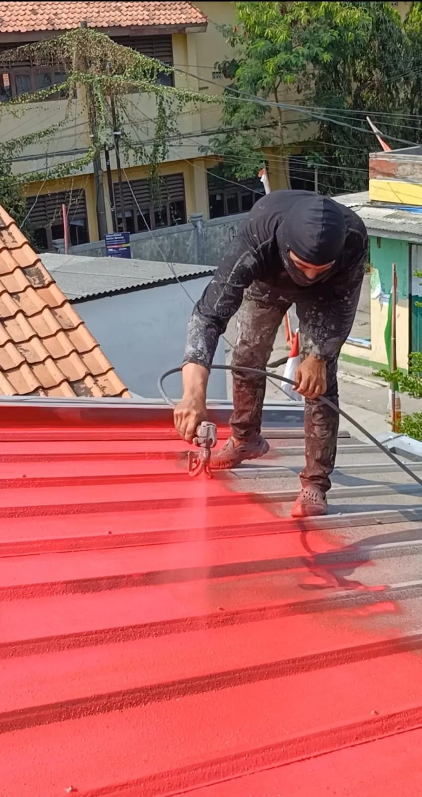Pekerja menyemprotkan coating merah pada permukaan atap spandek.