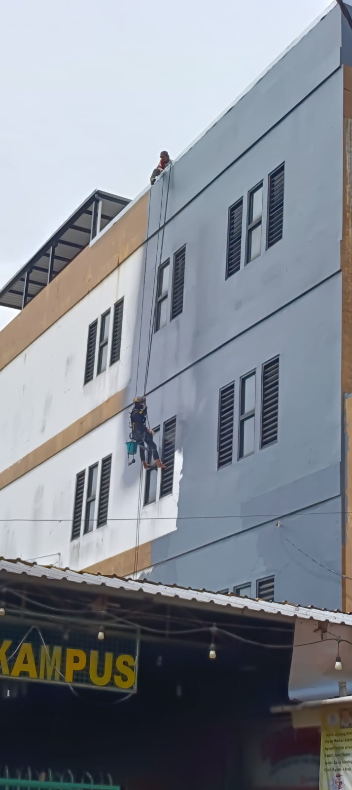 Pengerjaan coating dinding luar gedung dengan akses tali
